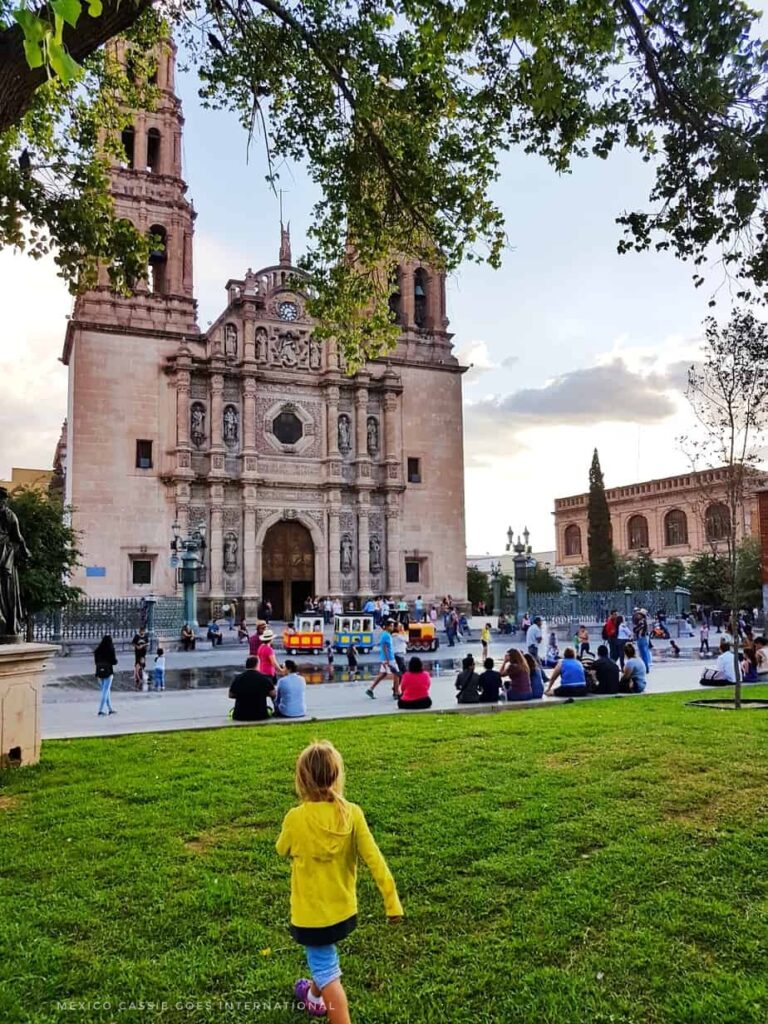 small child in yellow shirt walking on grass. large church in background