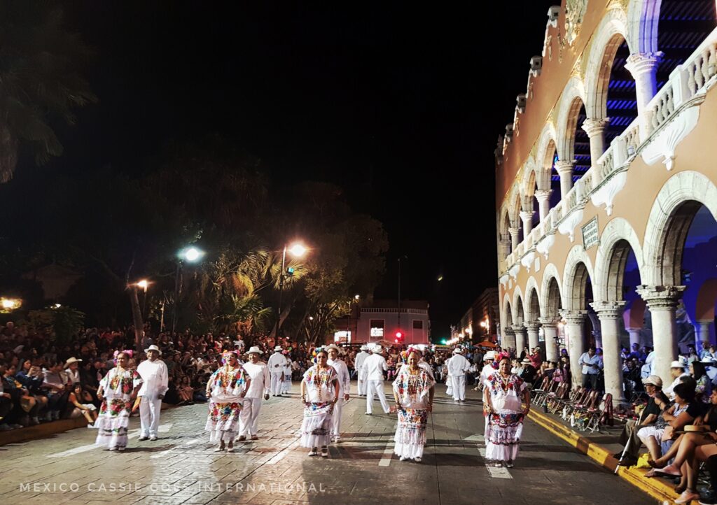 night scene, people in white traditional clothes dancing by arches of a building