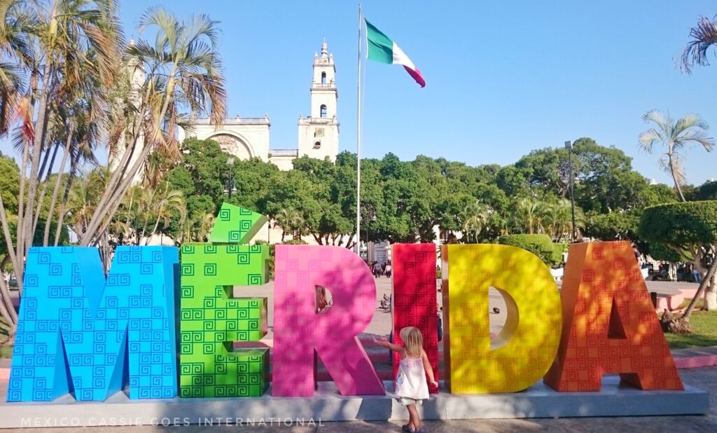 little girl standing in front of merida letters, church and flag in background