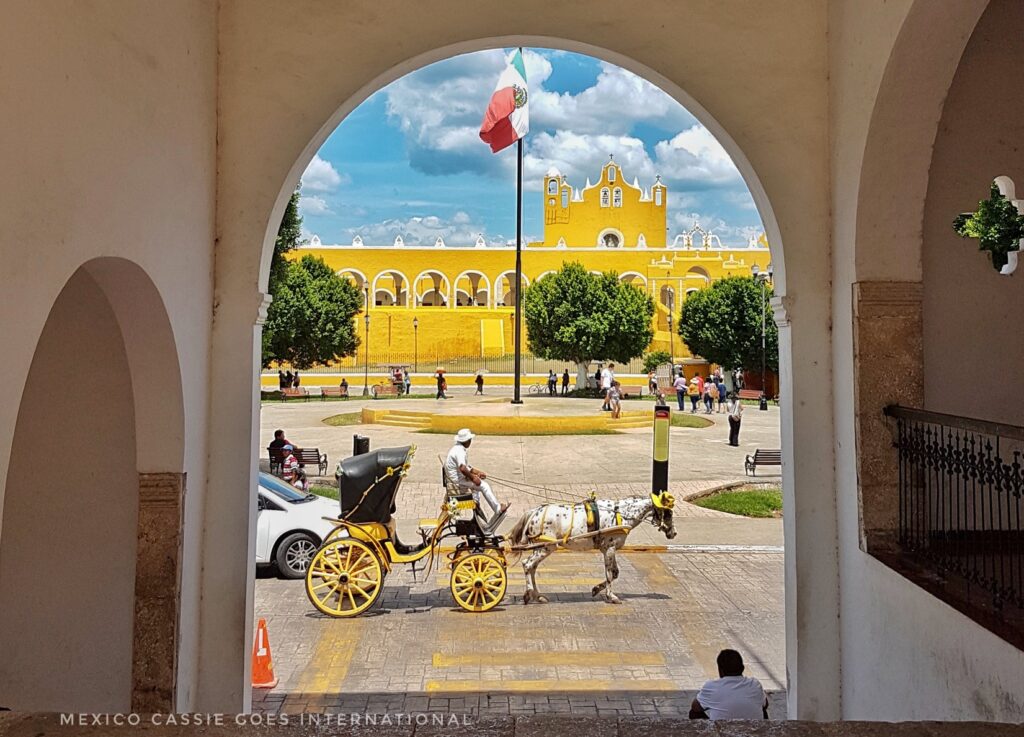 view through arch - horse drawn carriage, mexican flag and the convent in the background
