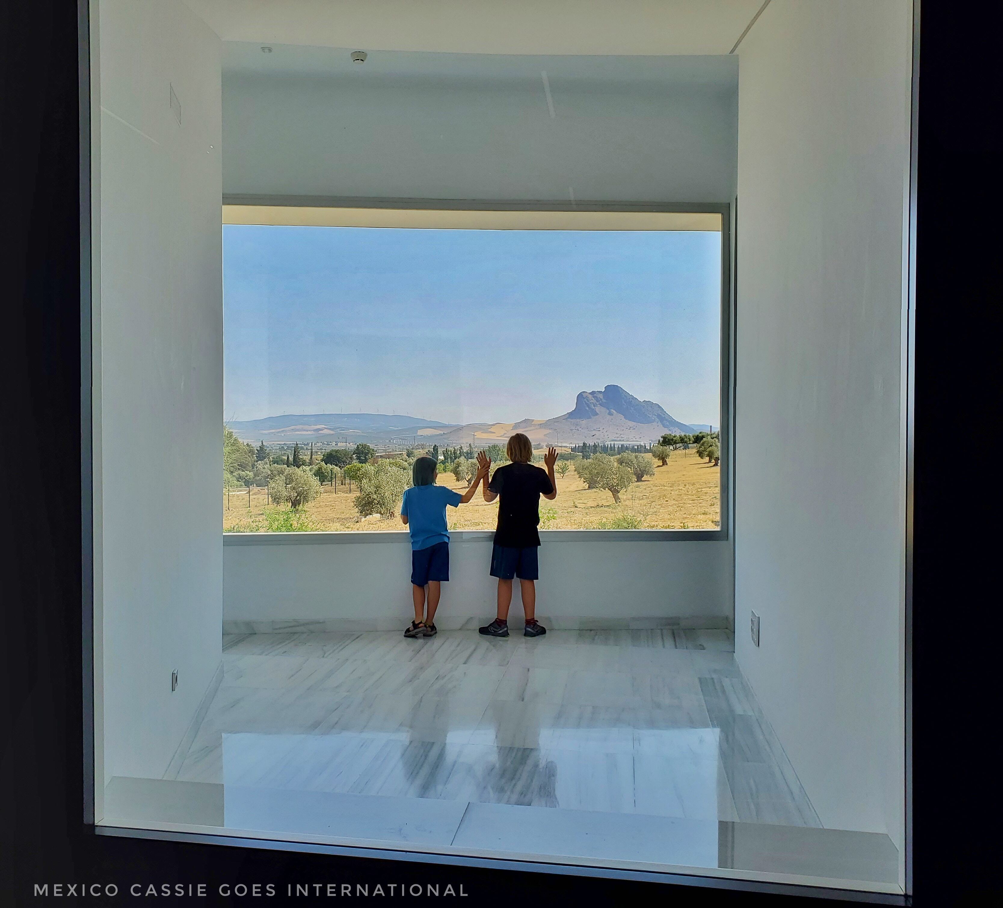 two children standing at a window looking at the prone face of the peña de los enamorados