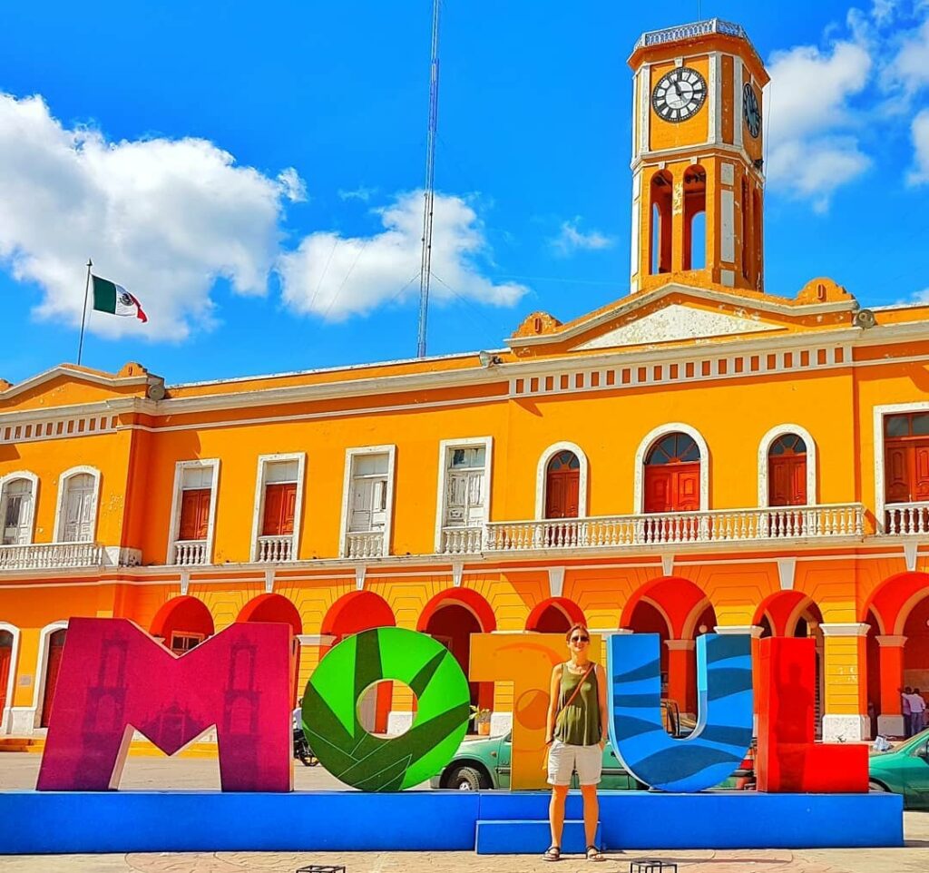 Motul letters, large yellow building behind with clock tower in middle. woman in green tshirt in front of letters