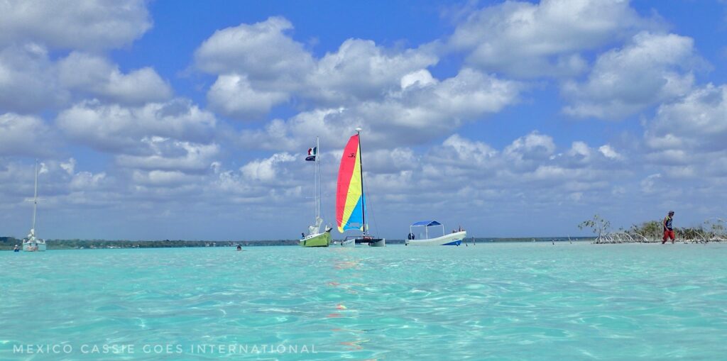 perfect light blue sea, blue sky, white clouds, sailing boat with red, yellow and blue sail
