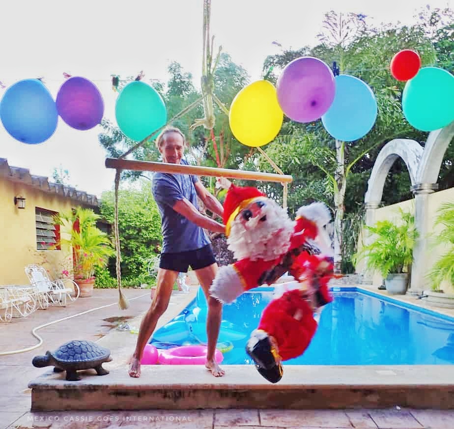 man on edge of pool hitting a santa piñata. balloons in a line