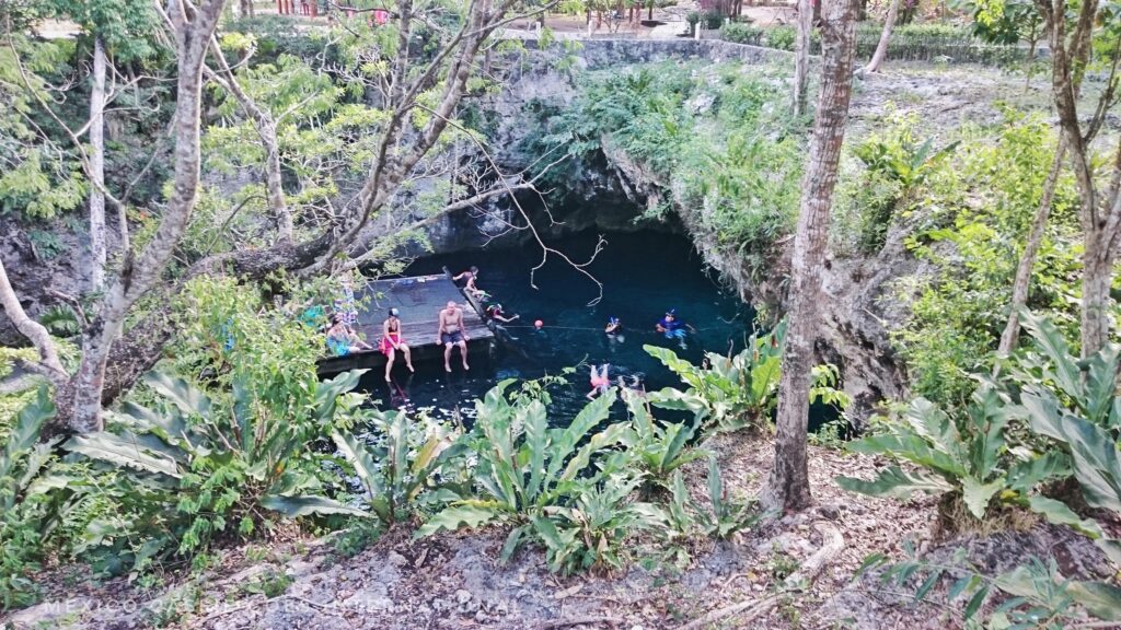 looking down into cenote - people sitting on platform, dark water