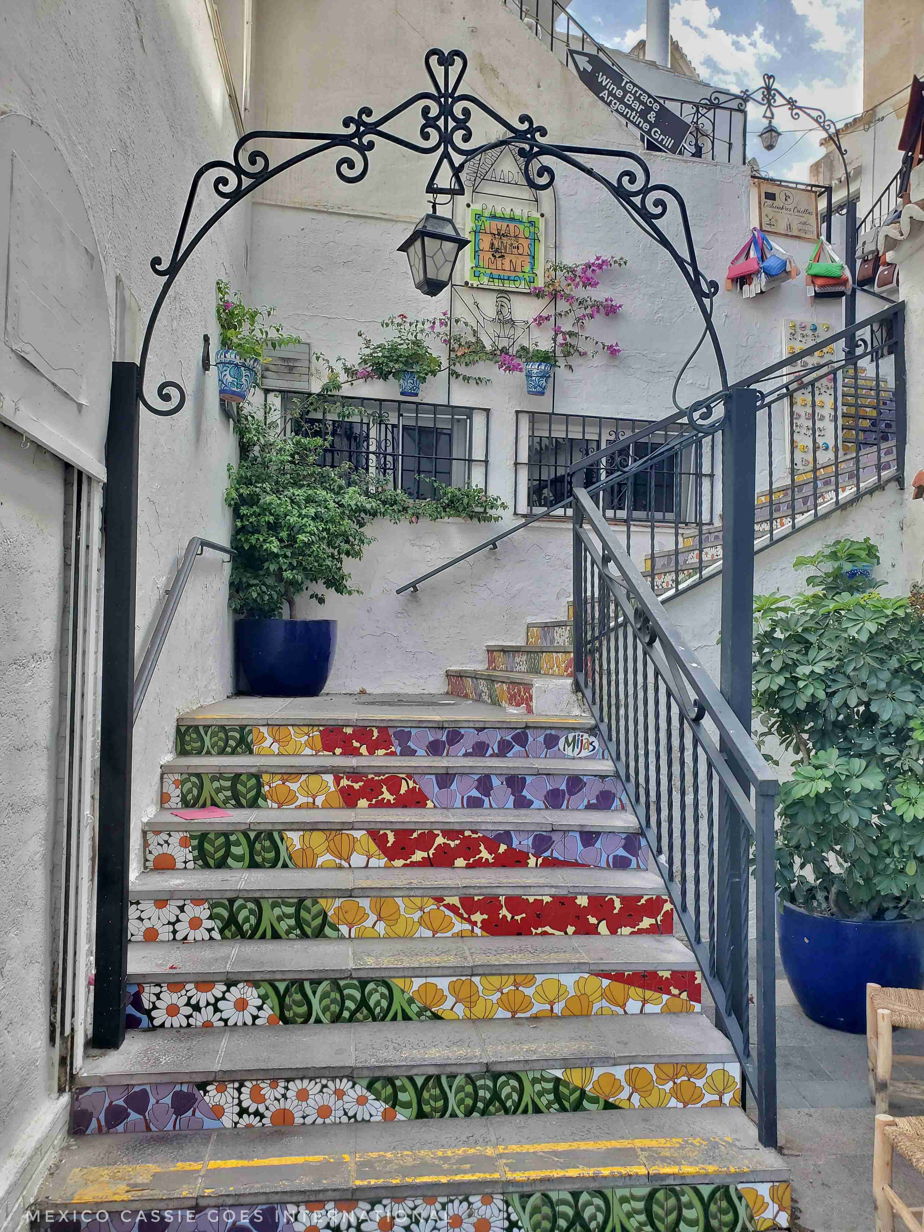 colourful steps - wrought iron arch, steps have white, green, yellow, red and blue in shape of upside down rainbow