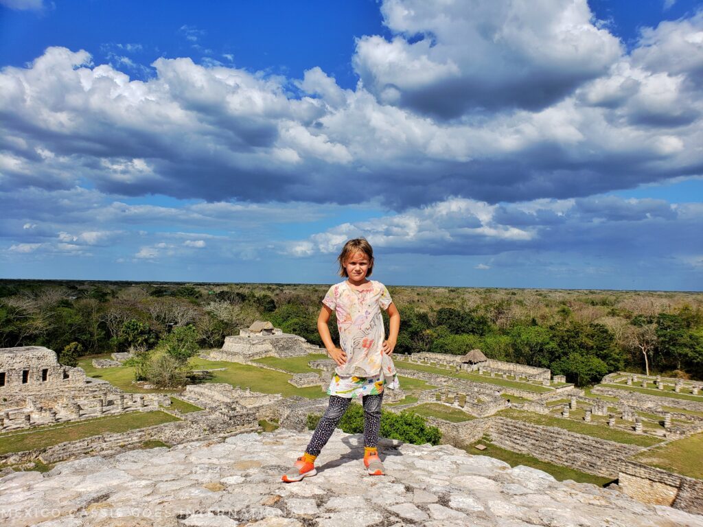 girl standing in front of camera, view over a mayan ruin behind her