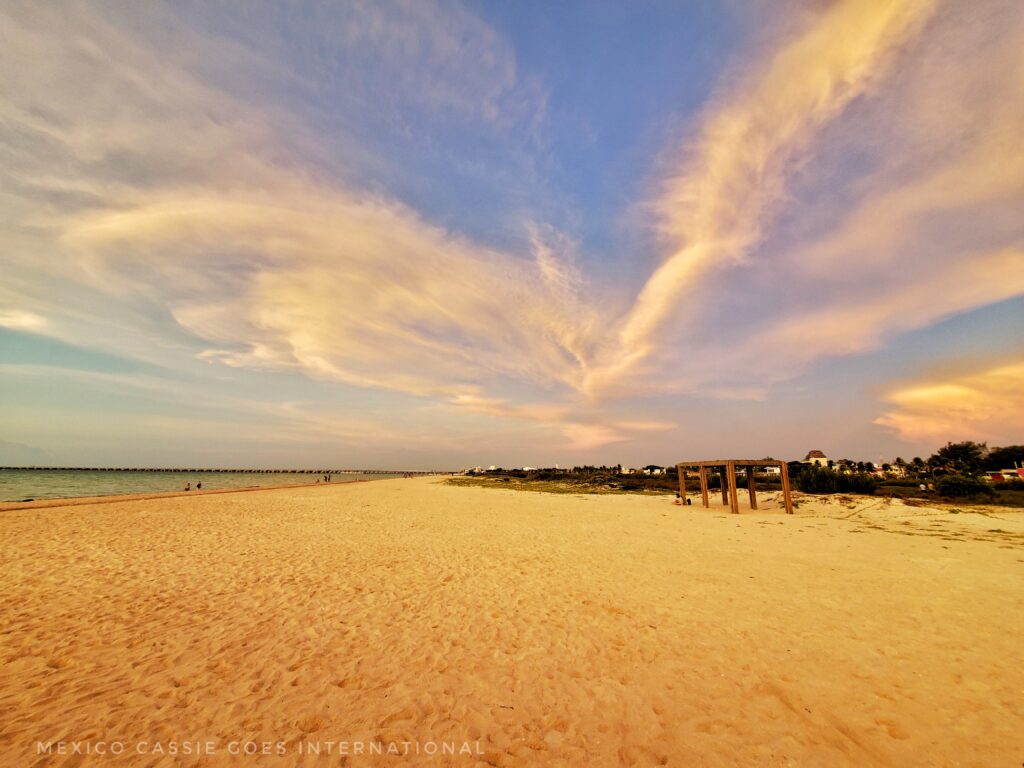 view of a near empty beach at dusk, sky has white clouds tinged with pink