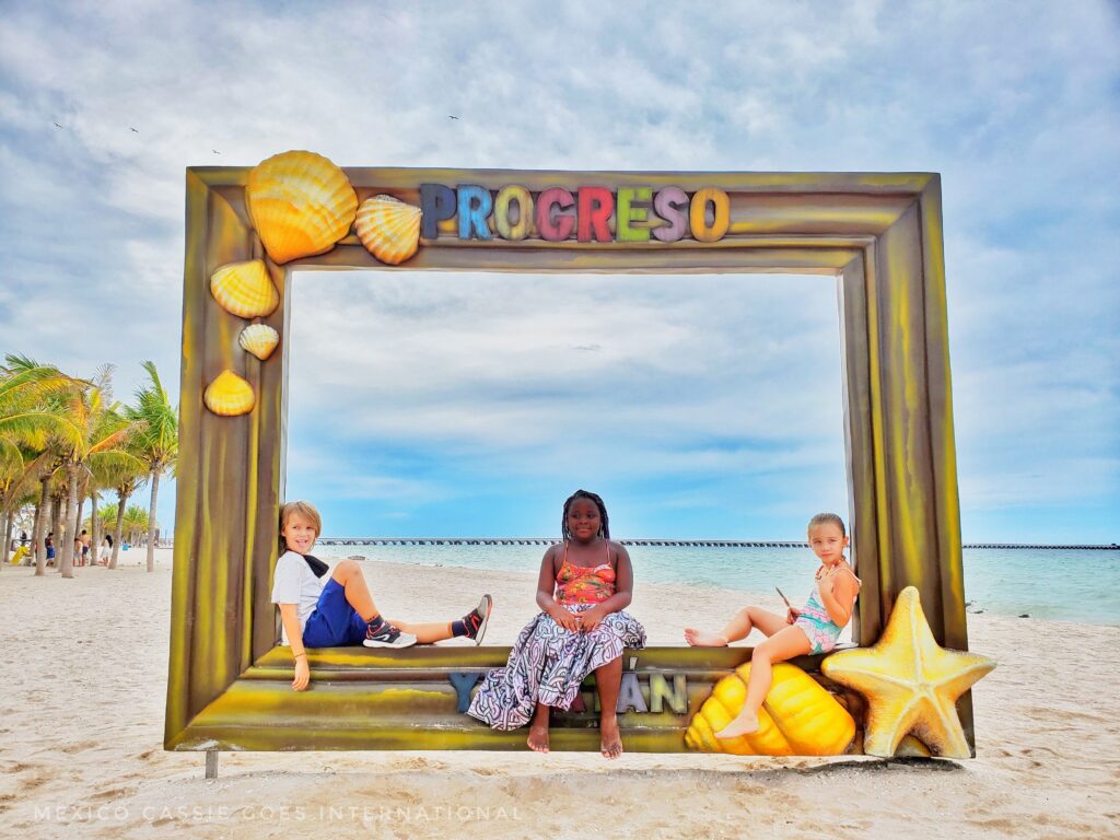 three children sitting on photo frame that saw progreso on a beach