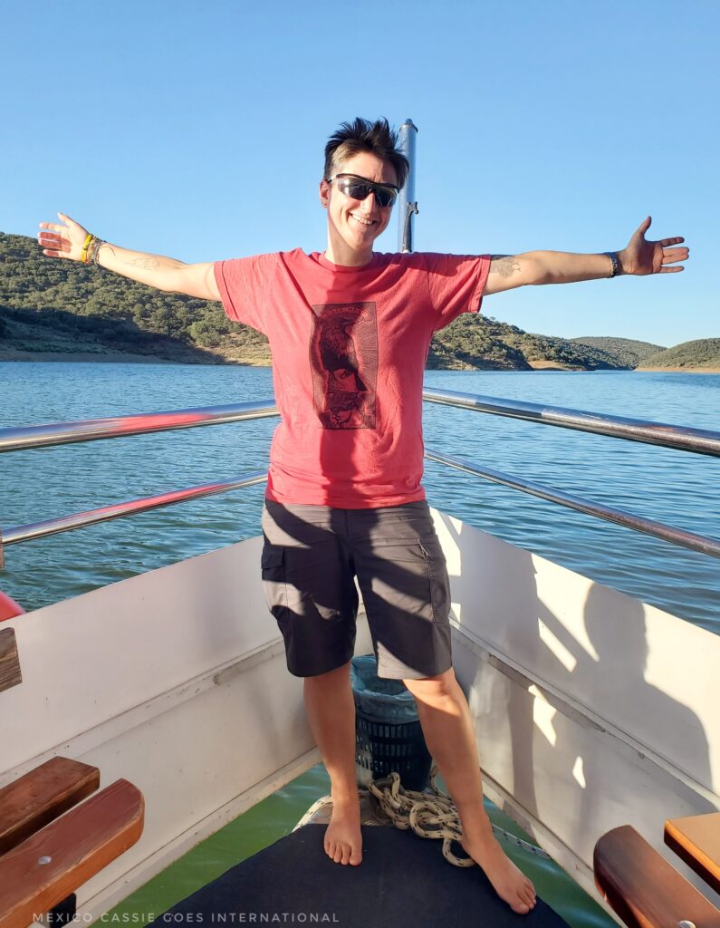 Cassie in a red tshirt standing at prow of boat with arms open wide