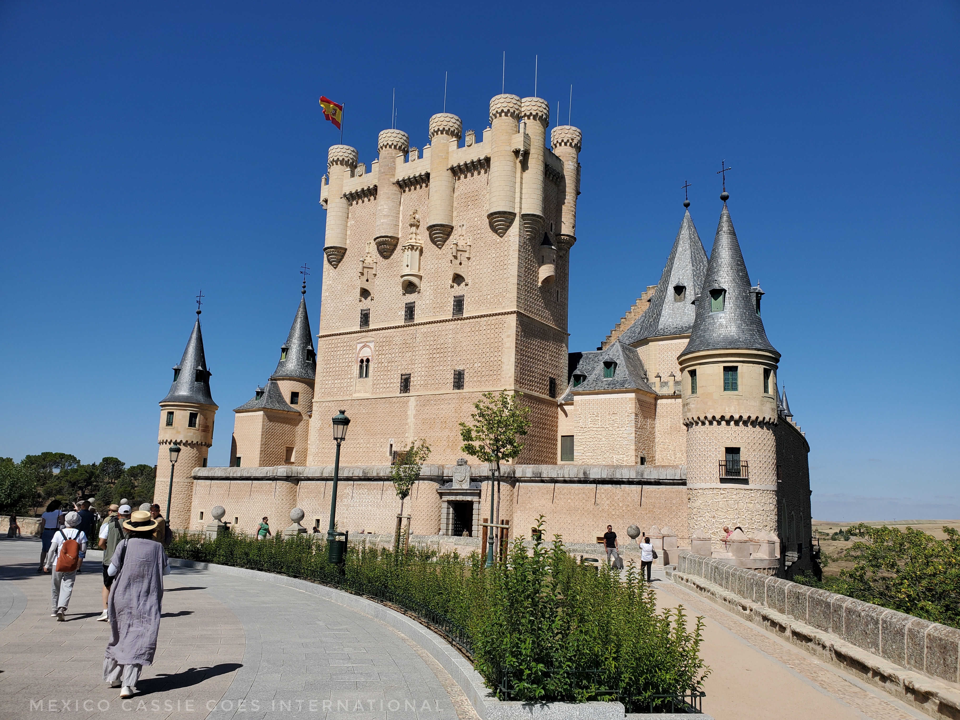 view of Segovia's Alcazar from the main approach. Torre del Homenaje in front with flag flying. Grey roofed turrets on each corner