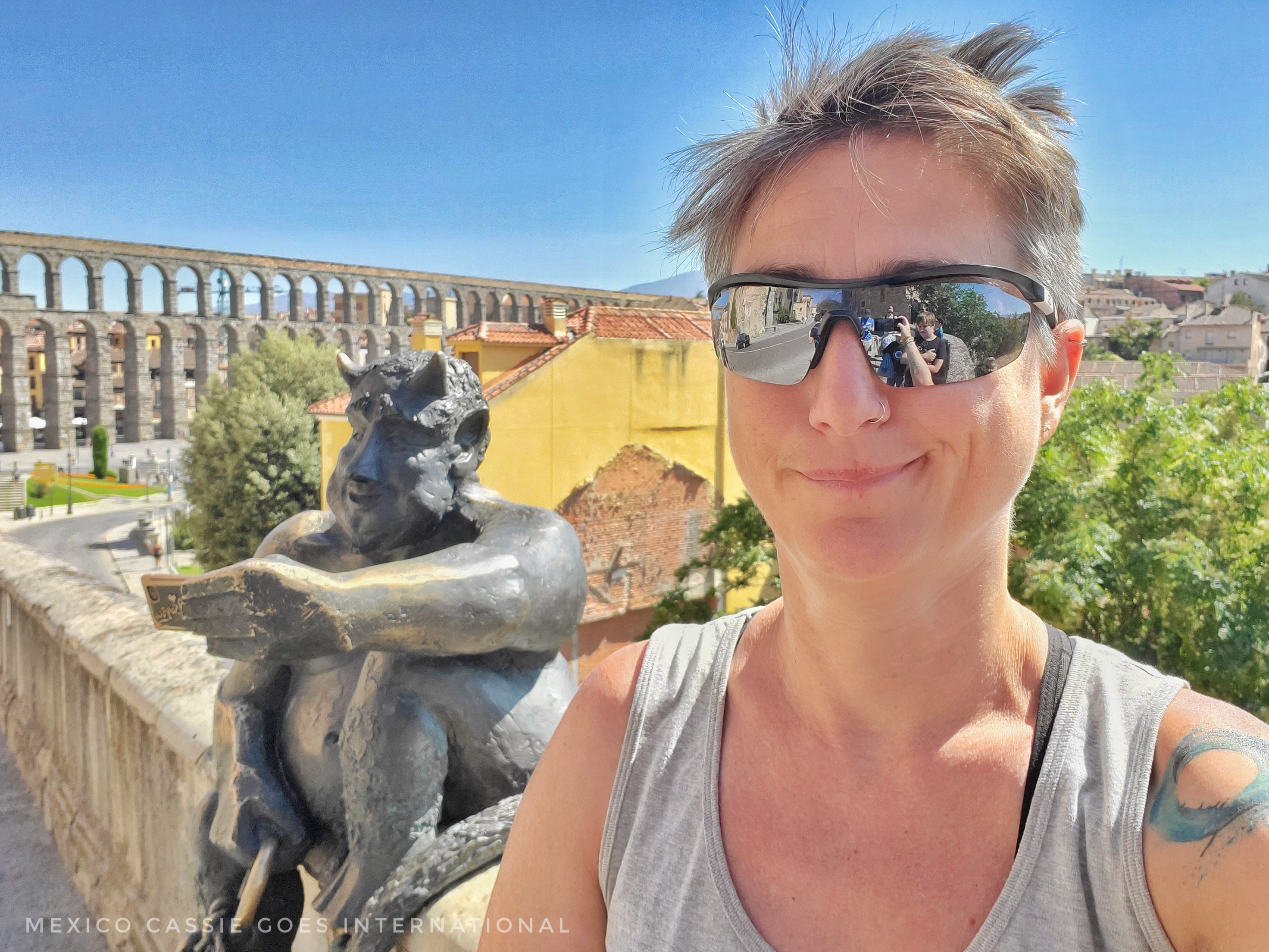 Cassie in sunglasses and grey tshirt with diablo sculpture (he's small and holding a phone). Aqueduct in background