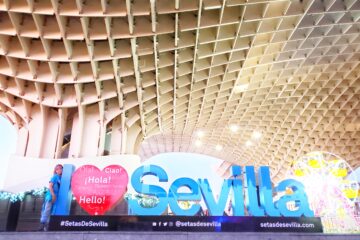 I ❤️ Sevilla in large letters with kid standing next to the I. Wooden criss cross sculpture in background