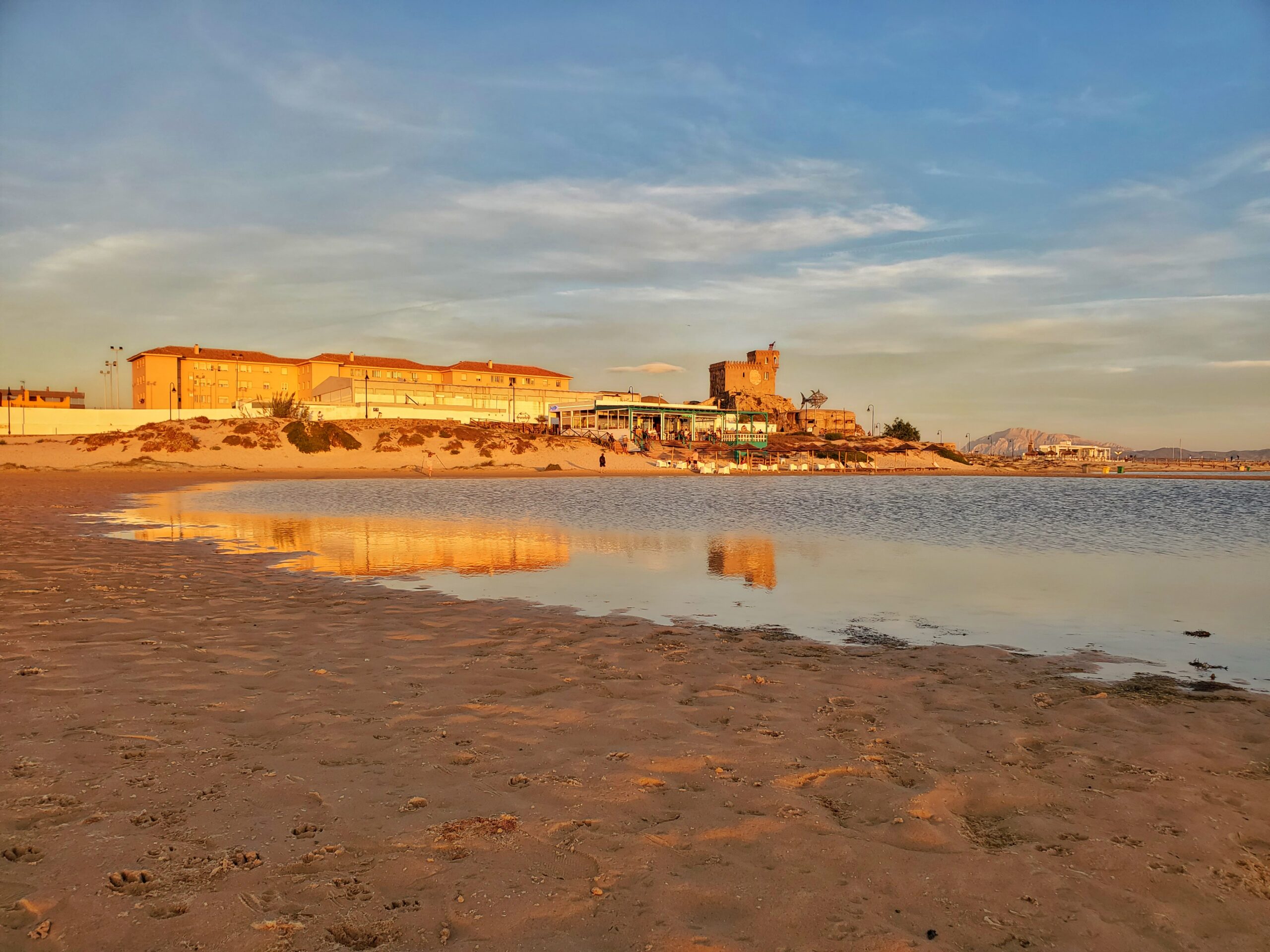 view of tarifa at sunset from beach with reflection of buildings in water