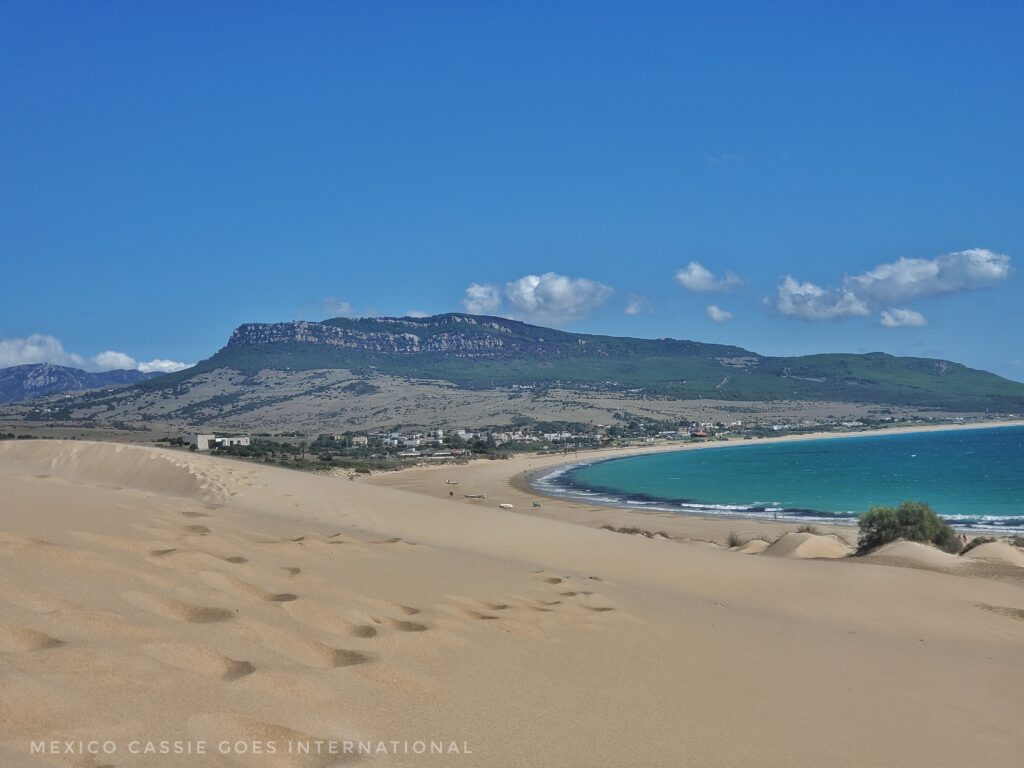 view of bolonia beach from top of dunes. footsteps in sand and green cliffs in distance
