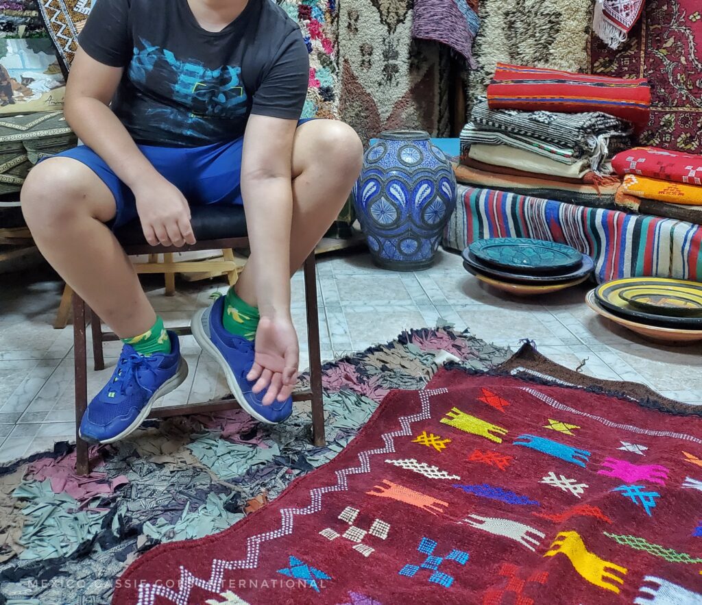 kid (photo cut off before head) on a stool, rugs on ground in front of kid