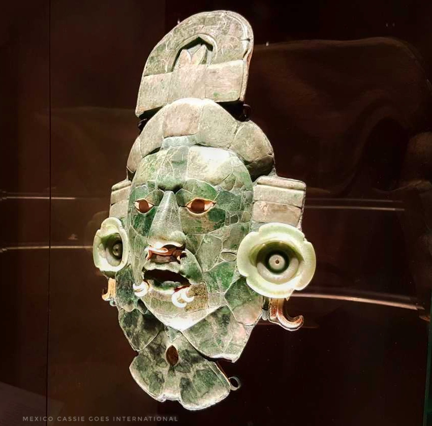 maya jade mask against a dark background. mask is made of pieces of green jade