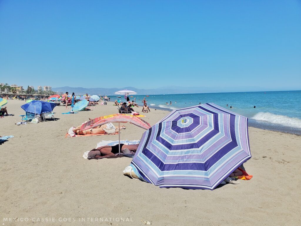 people lying behind umbrellas on a sunny, sandy beach