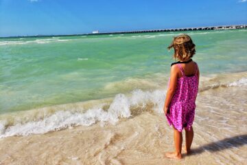 girl in pink dress standing looking at ocean - green water, blue sky