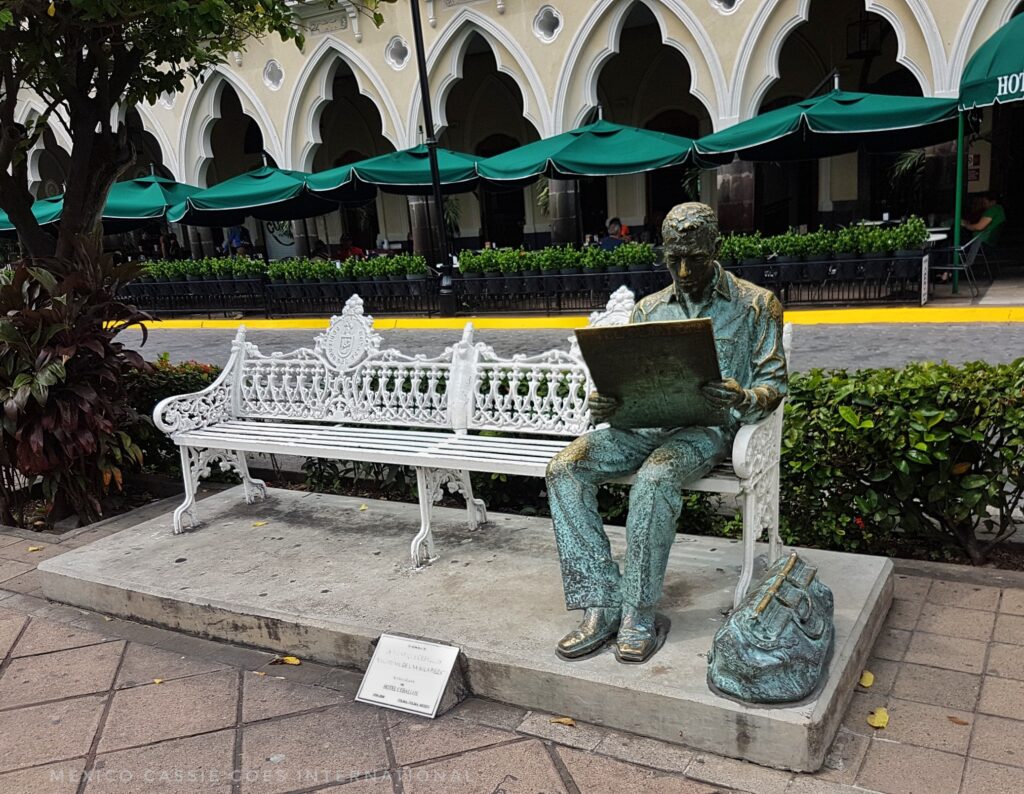 sculpture of a man on a bench reading a paper