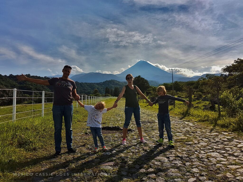 family (two adults two kids) holding hands across a cobbled road with a volcano in the distance