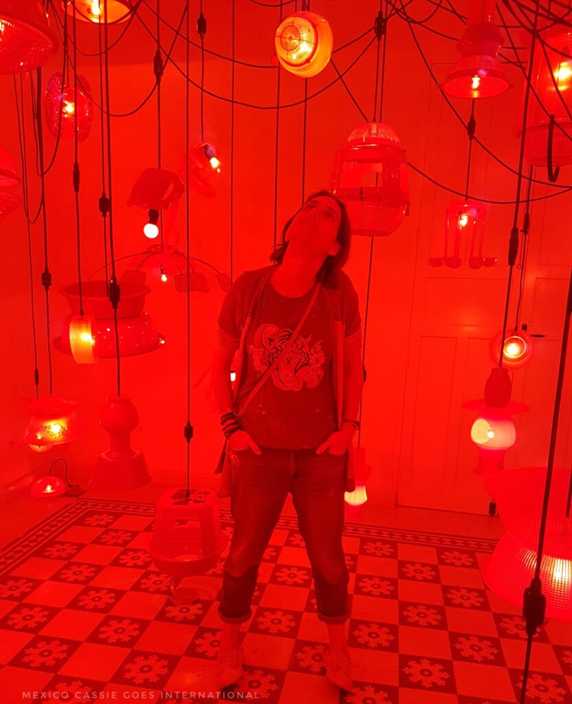 cassie standing surrounded by lights hanging down. entire picture is red