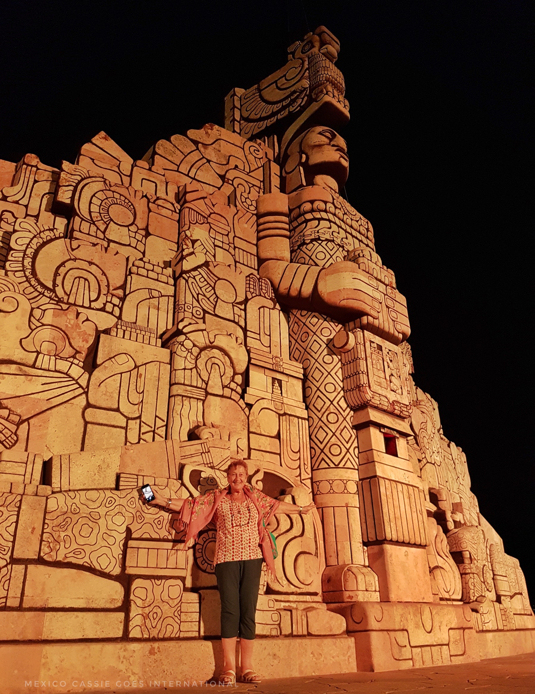 woman standing in front of large Mayan facade (the glorieta de la patria in merida)