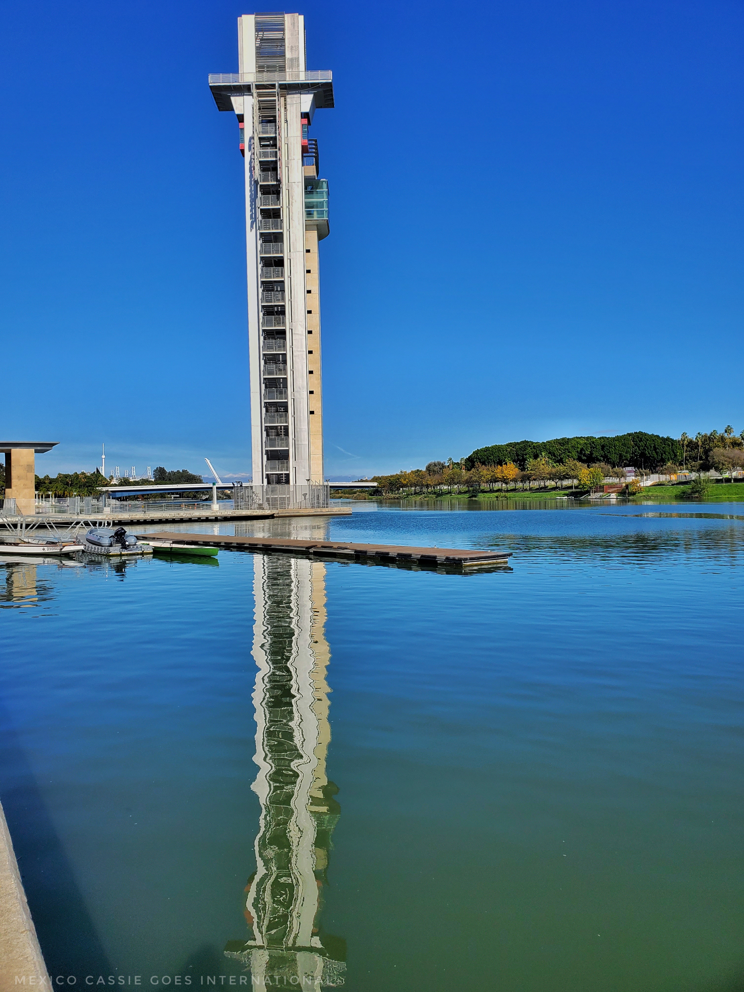 Torre Schindler (Sevilla tower) against blue sky. Reflected into water below