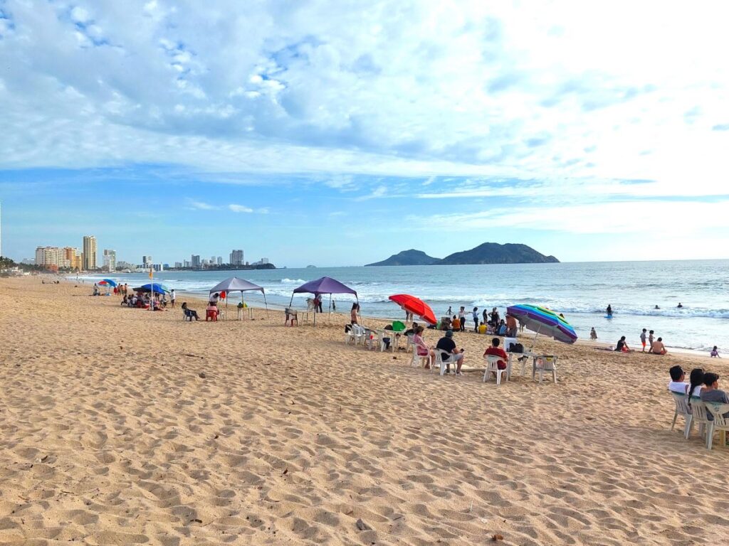 sandy beach, people under sun umbrellas, ocean and few small islands in distance