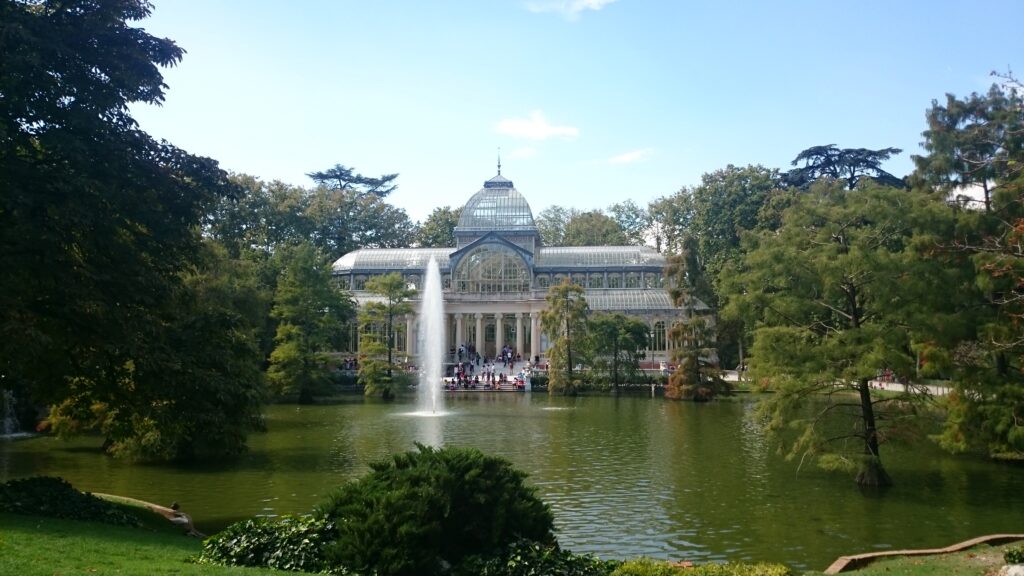 Madrid's palacio de cristal in summer, trees on left, fountain in lake