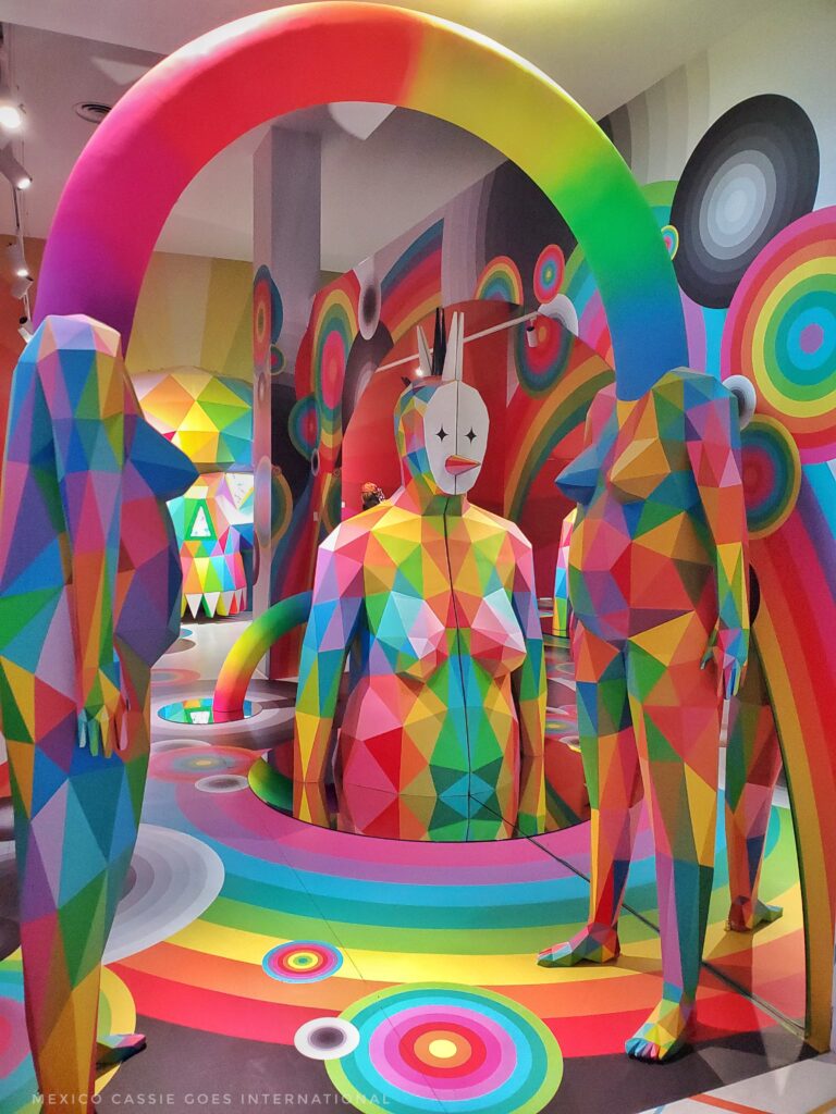 view of multicoloured sculptures of humans - front two are linked by a curved tube where heads should be