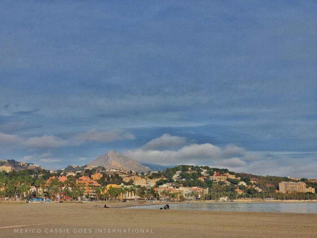 view of an empty Malaga beach with town and hills in distance