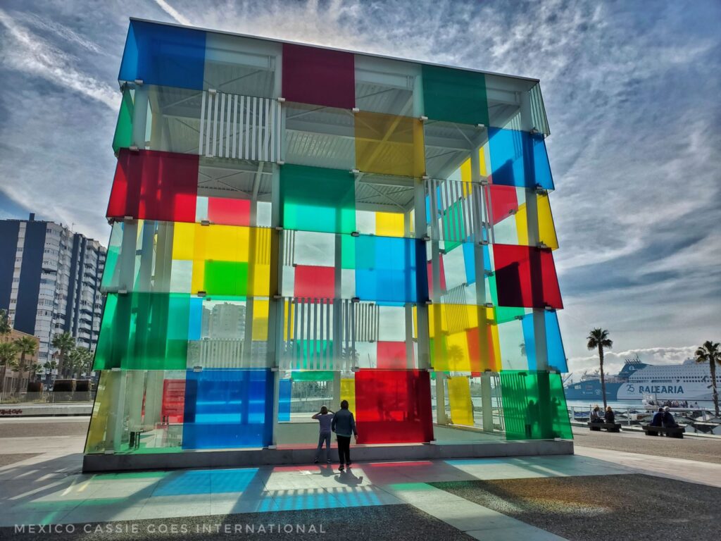 glass box building made up of coloured squares. reflections on floor, 2 kids standing at base