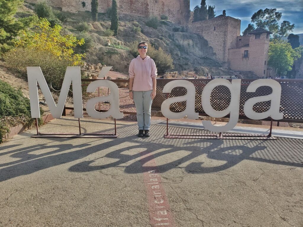 Large letters spelling Malaga but the L is replaced with an adult in a pink hoodie