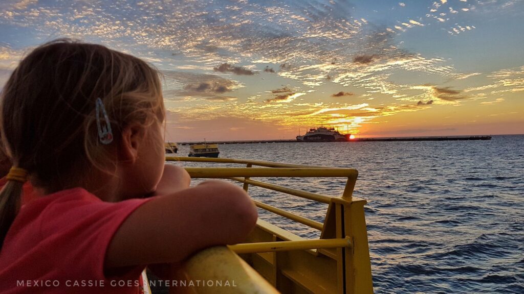 small child leaning on boat railing at sunset (sunset is visible)