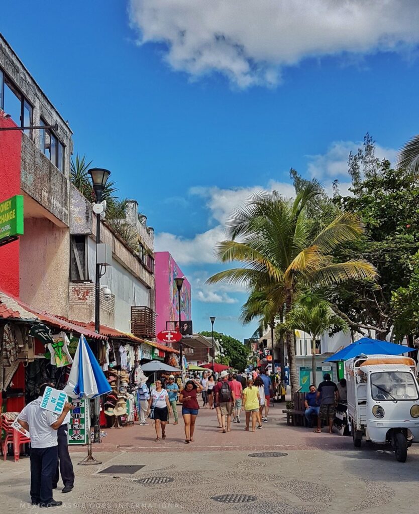 playa del carmen 5th avenue - brightly coloured buildings, palm trees and people milling around