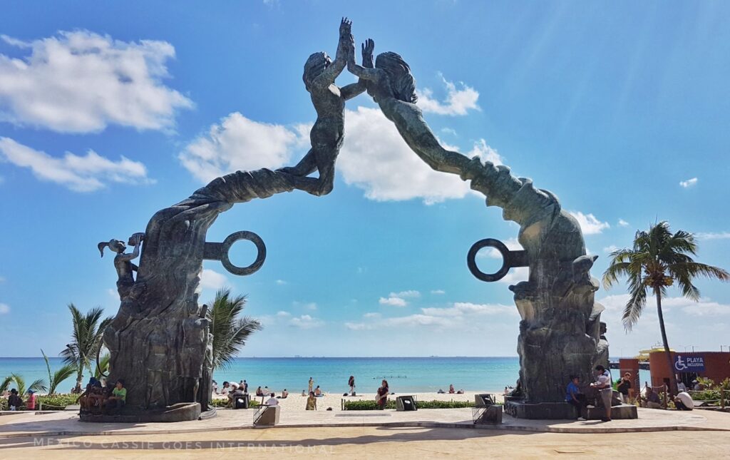 the sculpture on parque fundadores in Playa del Carmen - two separate sculptures that meet as mermaids with hands touching. Ocean behind