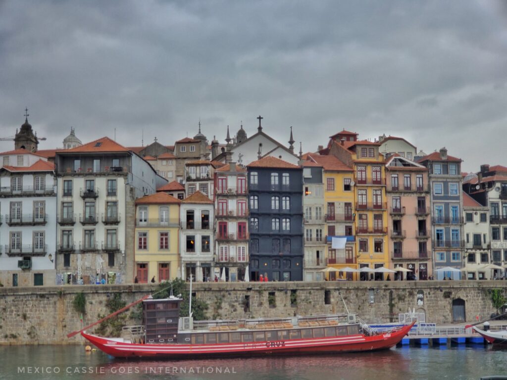 long red boat on river in front of a wall and very tall thin houses