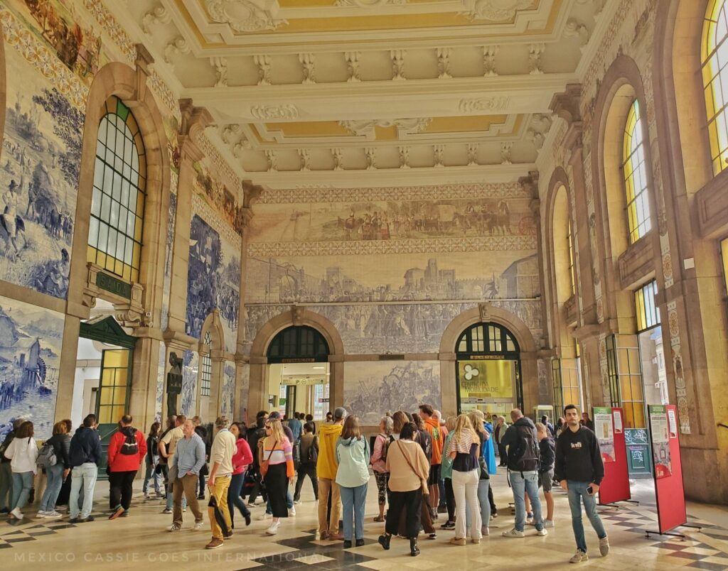 large hall - walls covered in blue and white tiled murals. people milling around