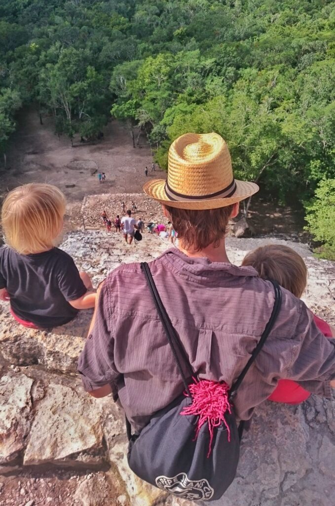 man in hat and two small children sitting at top of pyramid. photo taken from behind them looking down
