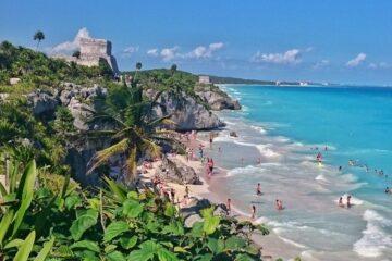view along the coast, turquoise water, beach, green vegetation and tulum ruins up on cliff