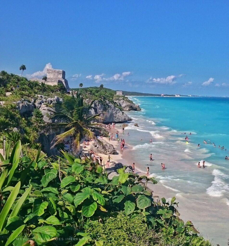 view along the coast, turquoise water, beach, green vegetation and tulum ruins up on cliff