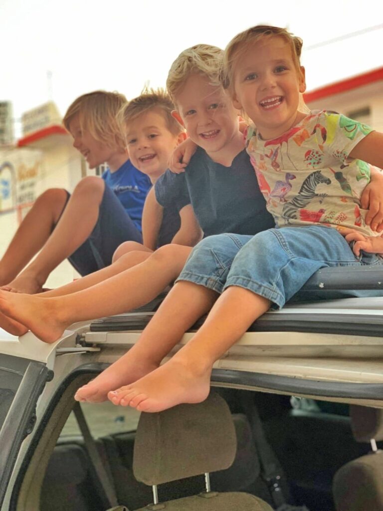 four small children sitting on roof of a car - 3 looking at camera and smiling