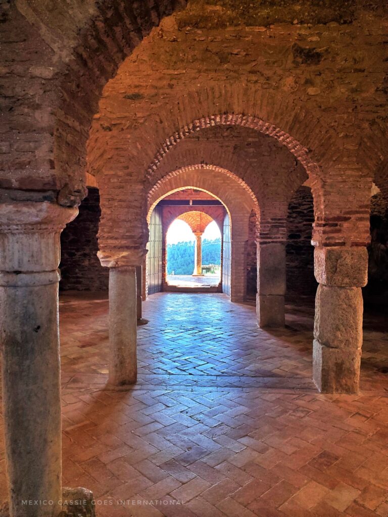 ancient arches in a room leading to open door at end where more arches and view over countryside