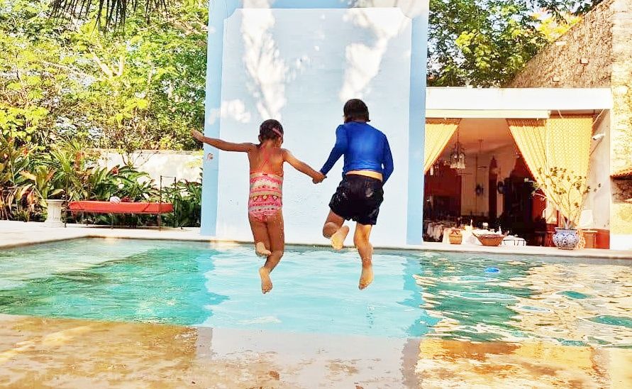 boy and girl holding hands while jumping into light blue pool water