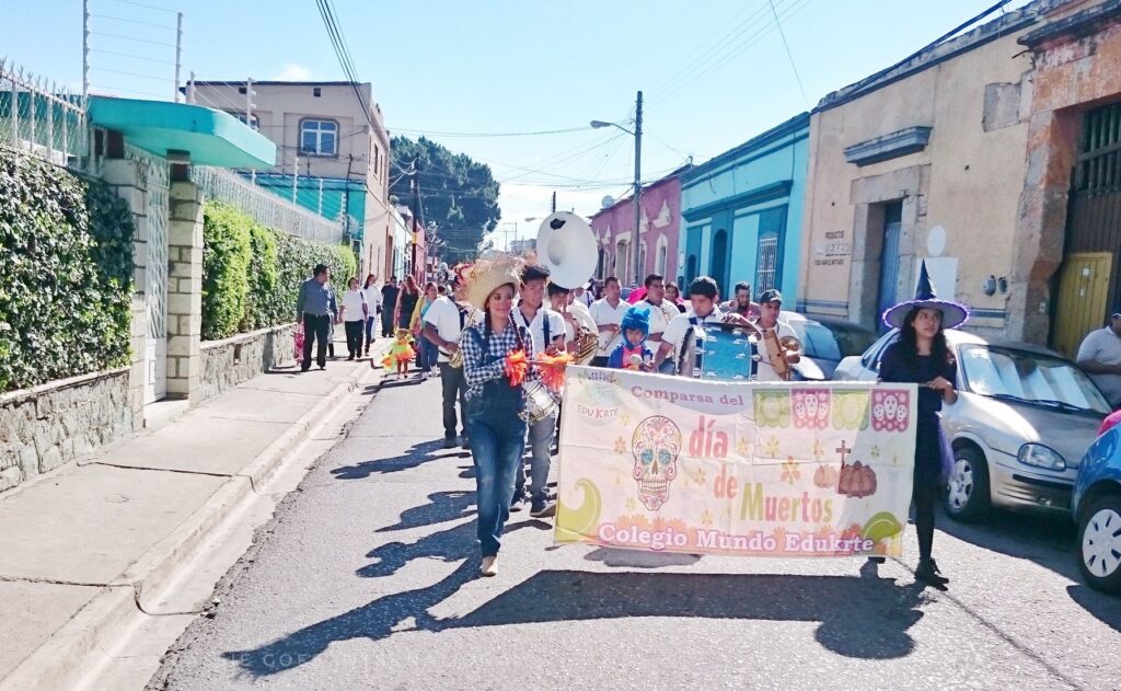 group of people marching down the road holding a sign between them a the front that reads dia de los muertos