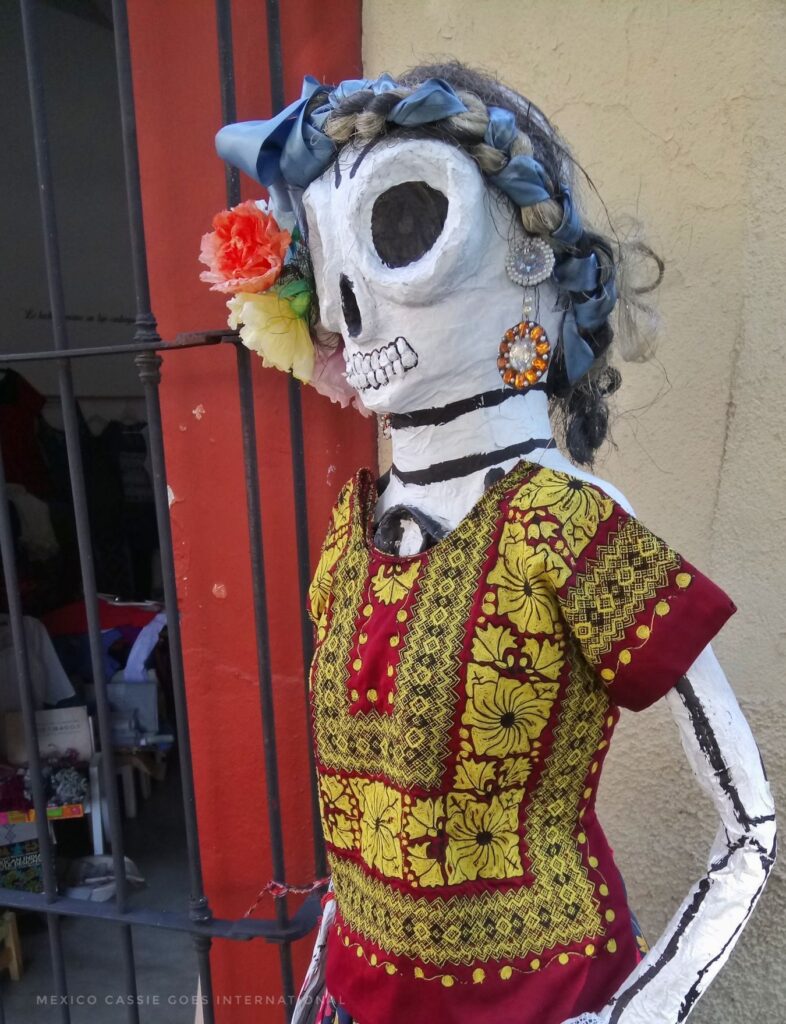 large papier mache skeleton in a traditional red Meixcan shirt