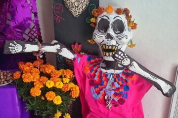 catrina in a bright pink shirt laughing and sitting next to marigolds