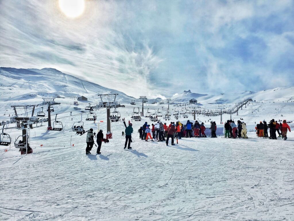 bright day up a mountain in Sierra Nevada, people standing around in distance, sun shining through clouds. cable car
