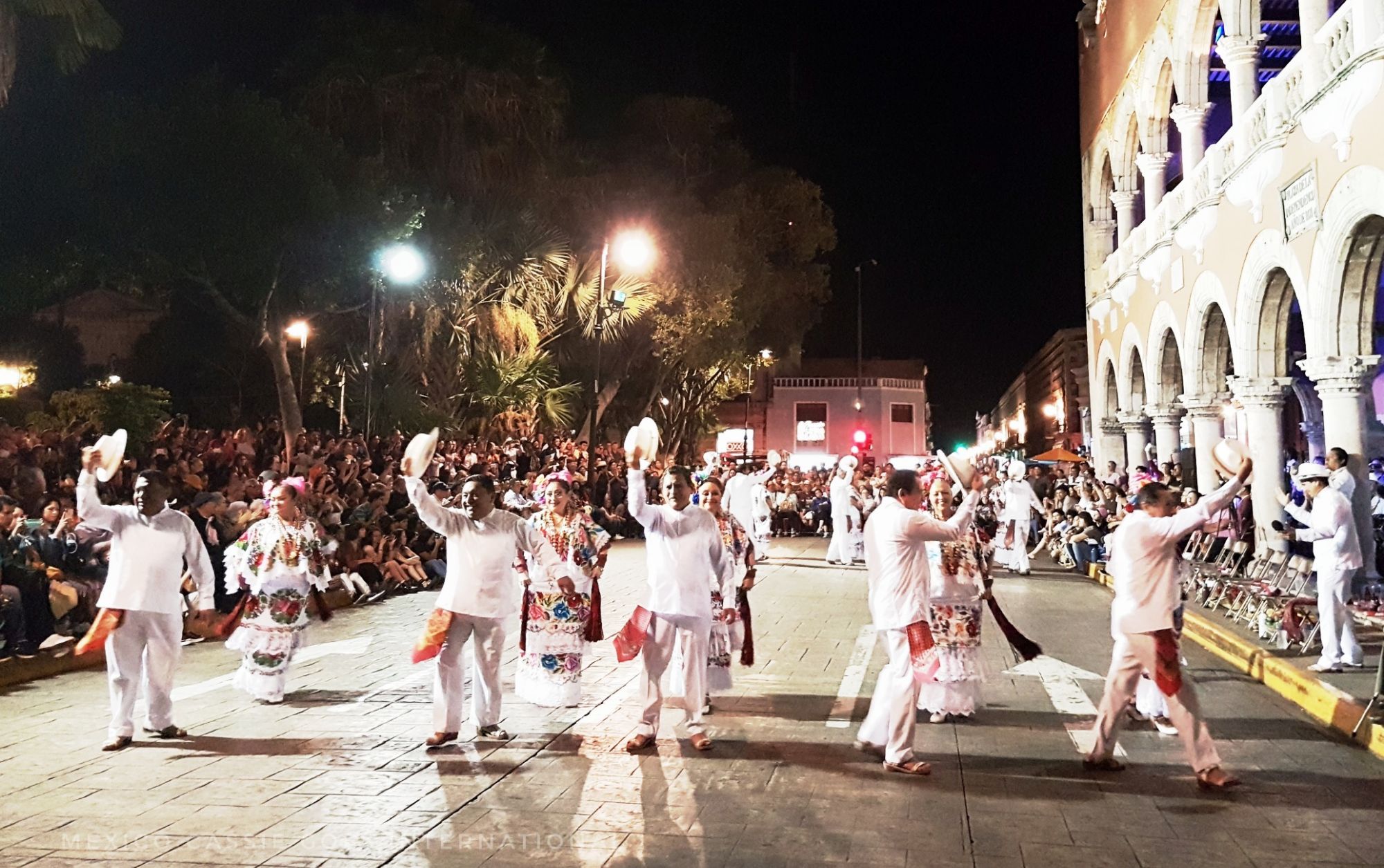 men and women in traditional Maya costume dancing in the street at night
